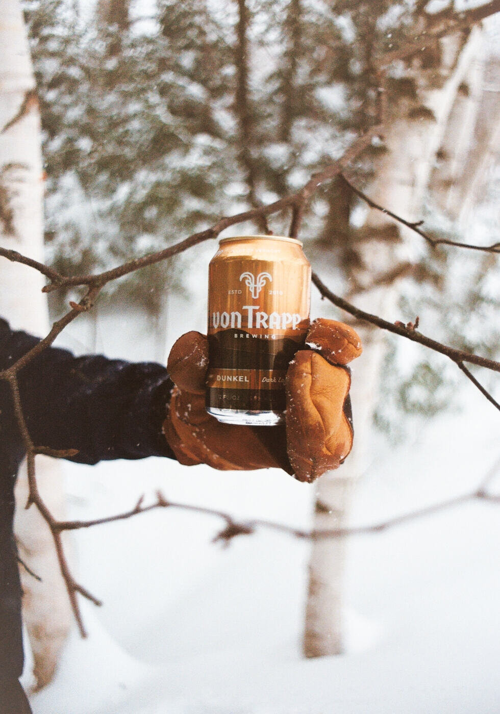 person holding a can of dunkel in snowy woods