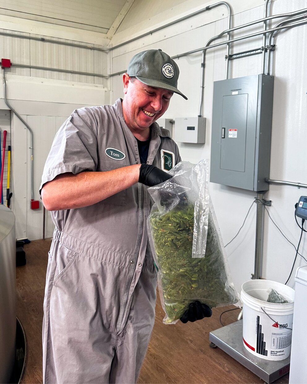 a man in a grey coverall holding a bag of green leaves