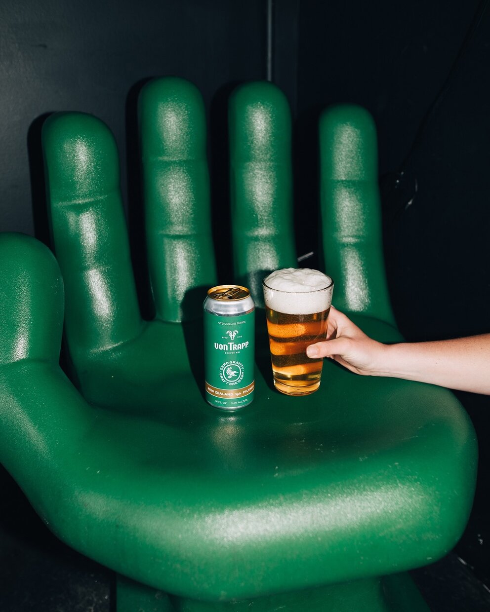 a hand holding a beer and a can on a green chair