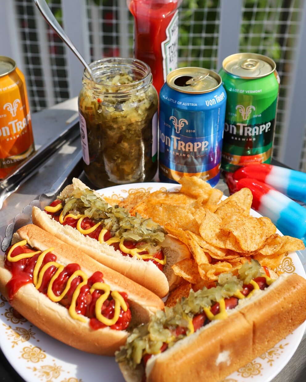 a plate of hot dogs and chips with condiments and a drink